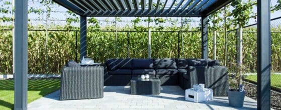 Moderne Pergola mit einem Sitzbereich aus schwarzen Möbeln und Rasenfläche im Hintergrund. | my-pergola24.com