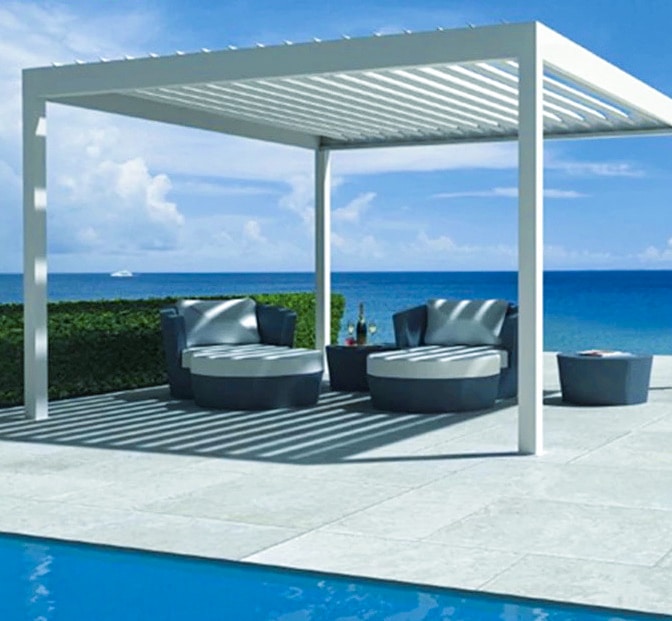 Moderne Pergola mit grauen Sitzmöbeln und Blick auf das Wasser unter einem blauen Himmel. | my-pergola24.com