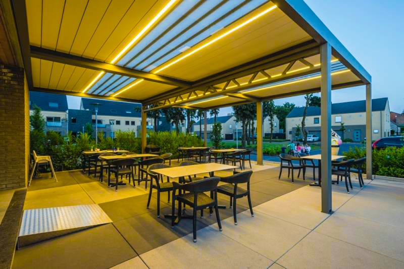 Lamellendach mit LED-Beleuchtung über einer Gastronomie-Terrasse in der Abenddämmerung