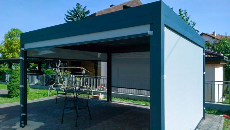 Lamellendach mit Stoffseitenteilen über gepflasterter Terrasse an einem Einfamilienhaus