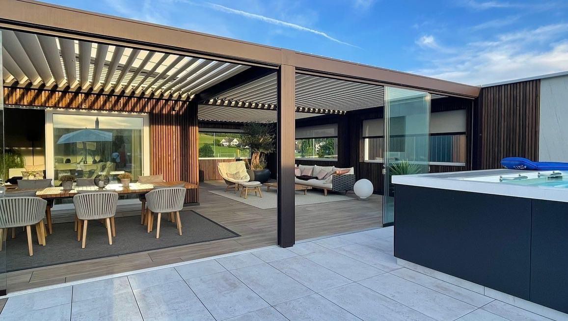 Lamellendach in Holzoptik mit Glas-Schiebeelementen über einer Dachterrasse mit Essplatz und Whirlpool