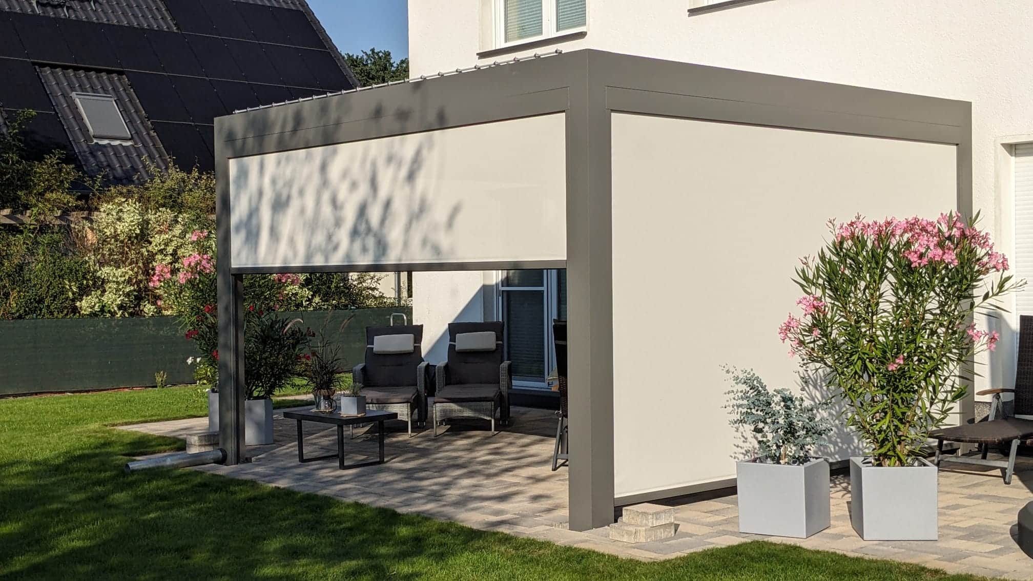 Graues Lamellendach mit ZIP-Screens an zwei Seiten über einer gepflasterten Gartenterrasse
