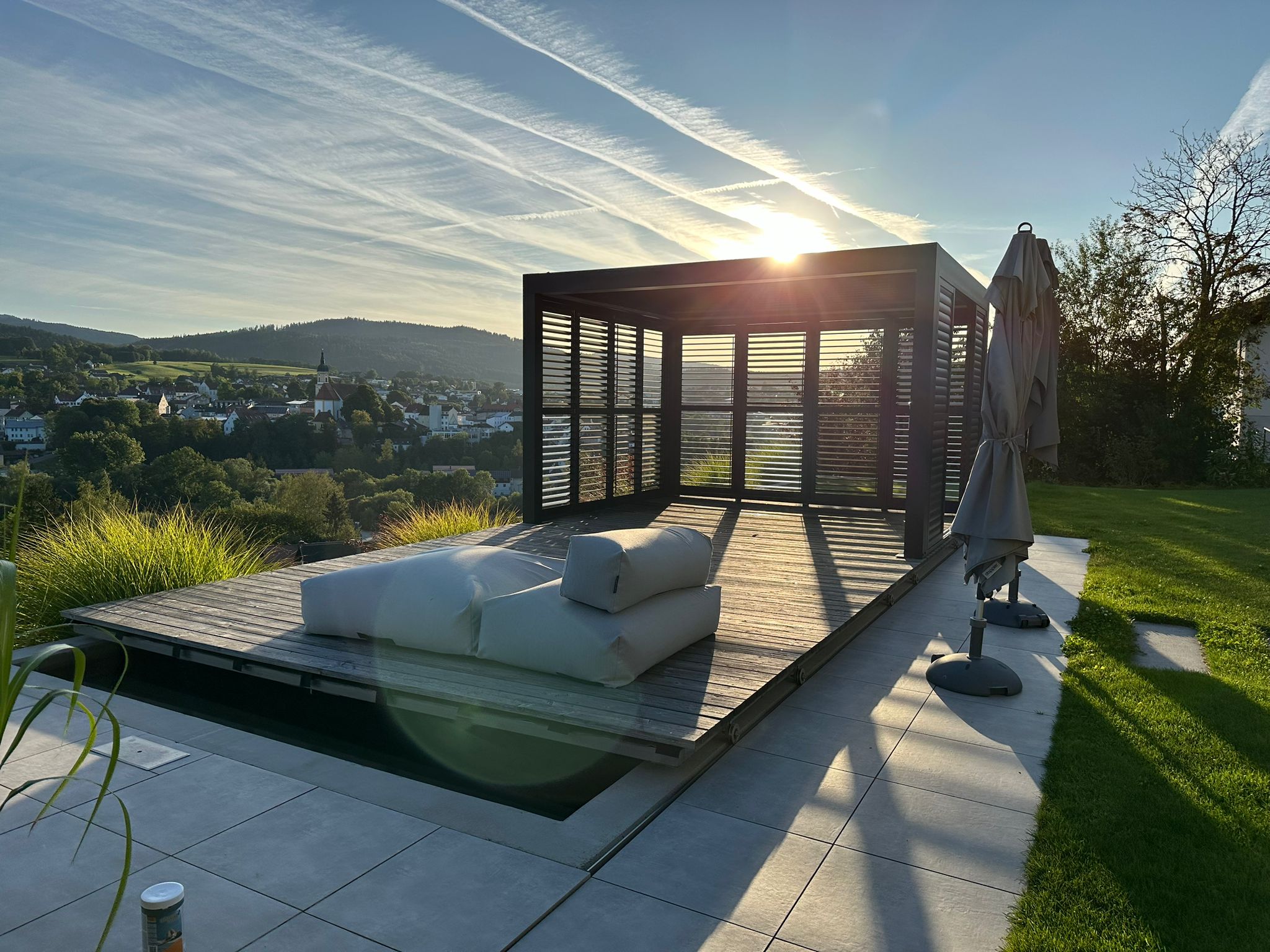 Anthrazitfarbene Pergola mit Lamellen-Seitenelementen im Abendlicht über dem Pool