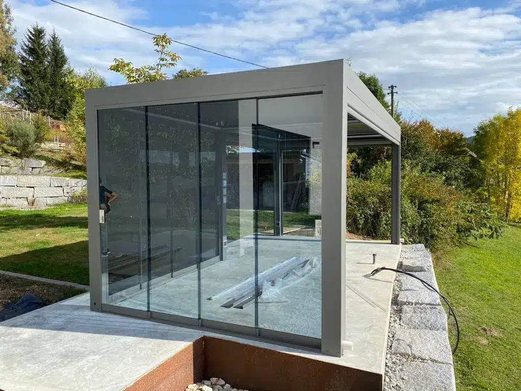 Moderne Pergola mit Glaswänden und Aluminiumrahmen in einem Gartenbereich. | my-pergola24.com
