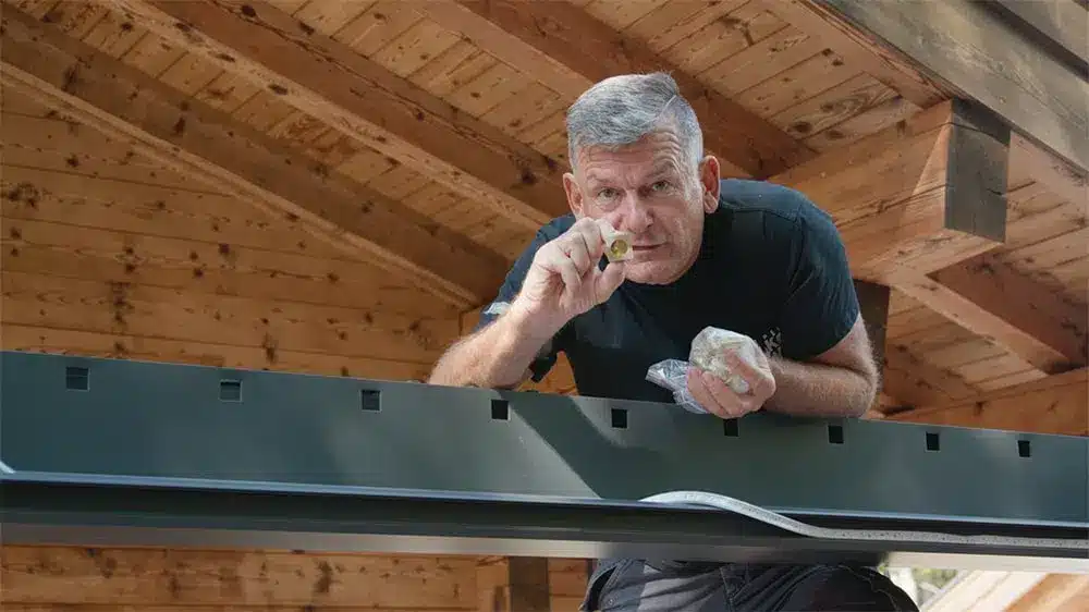 Mann, der eine Pergola montiert und dabei einen kleinen Gegenstand in der Hand hält. | my-pergola24.com