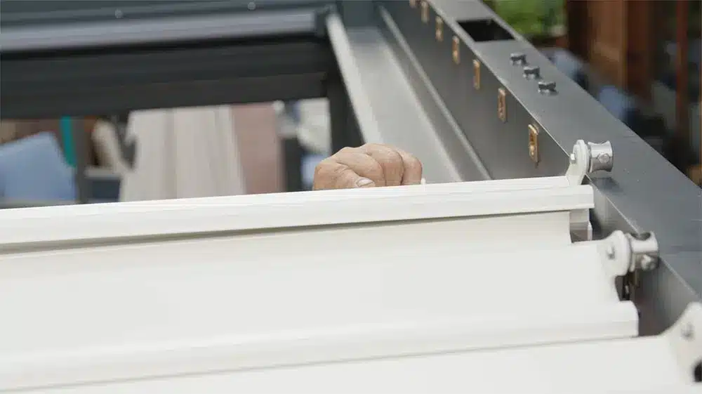 Eine Hand, die eine Beschattungseinheit an einer Pergola justiert, um den Schatten zu regulieren. | my-pergola24.com