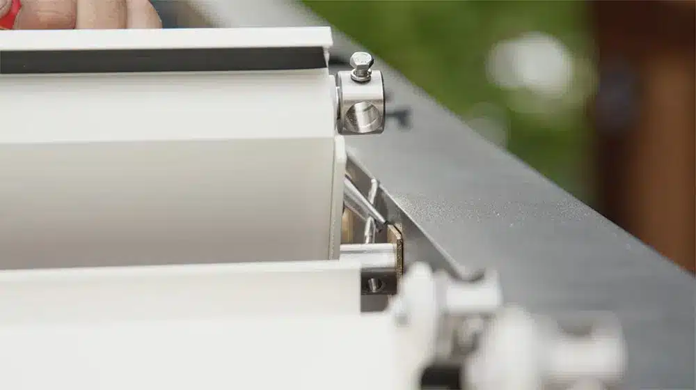 Detailaufnahme eines Rollmechanismus für eine Pergola mit weißen Stoffbahnen und Metallkomponenten. | my-pergola24.com