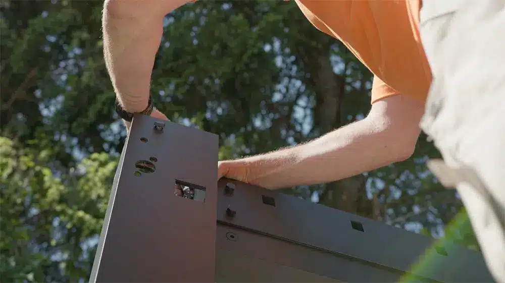 Eine Person befestigt ein Pergola-Element mit einem Werkzeug im Freien. | my-pergola24.com