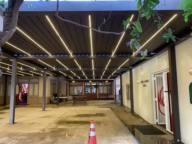 Großes Lamellendach über einem Hof am Abend. Zwischen den Lamellen leuchten LED-Leisten