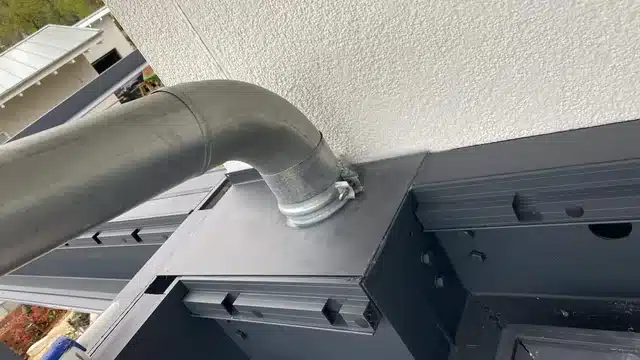 Detail: Fallrohr mit Anschluss am Rahmen eines Lamellendachs direkt an der Hauswand