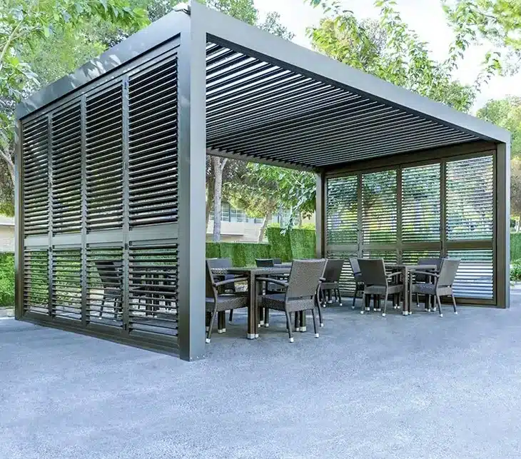 Moderne Pergola mit horizontalen Lamellen und einem Sitzbereich aus Stühlen und Tischen. | my-pergola24.com