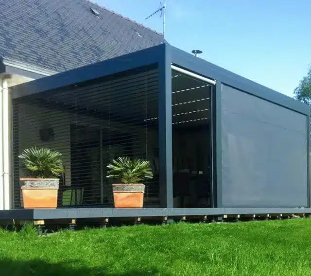 Pergola mit Lamellendach in Anthrazit und Screen-Seitenwand auf einem Holzdeck im Garten