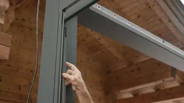 Montage der ZIP-Screens am Pfosten eines anthrazitfarbenen Lamellendachs an einem Holzhaus