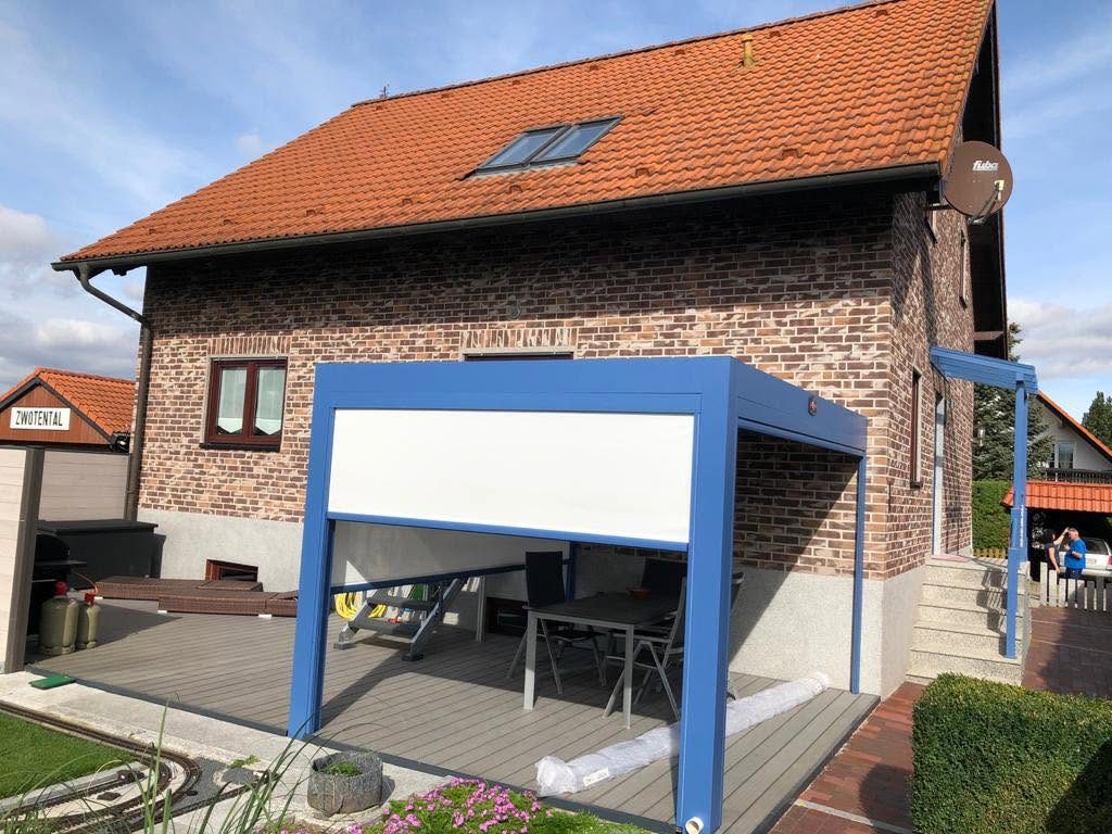 Backsteinhaus mit blauer Pergola und weißem Screen an der Terrasse, davor ein Blumenbeet