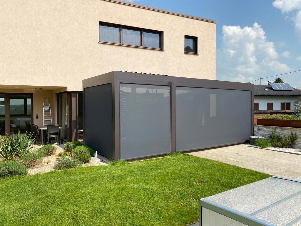 Haus mit beiger Fassade und anthrazitfarbenem Lamellendach mit Screens, davor ein Rasen