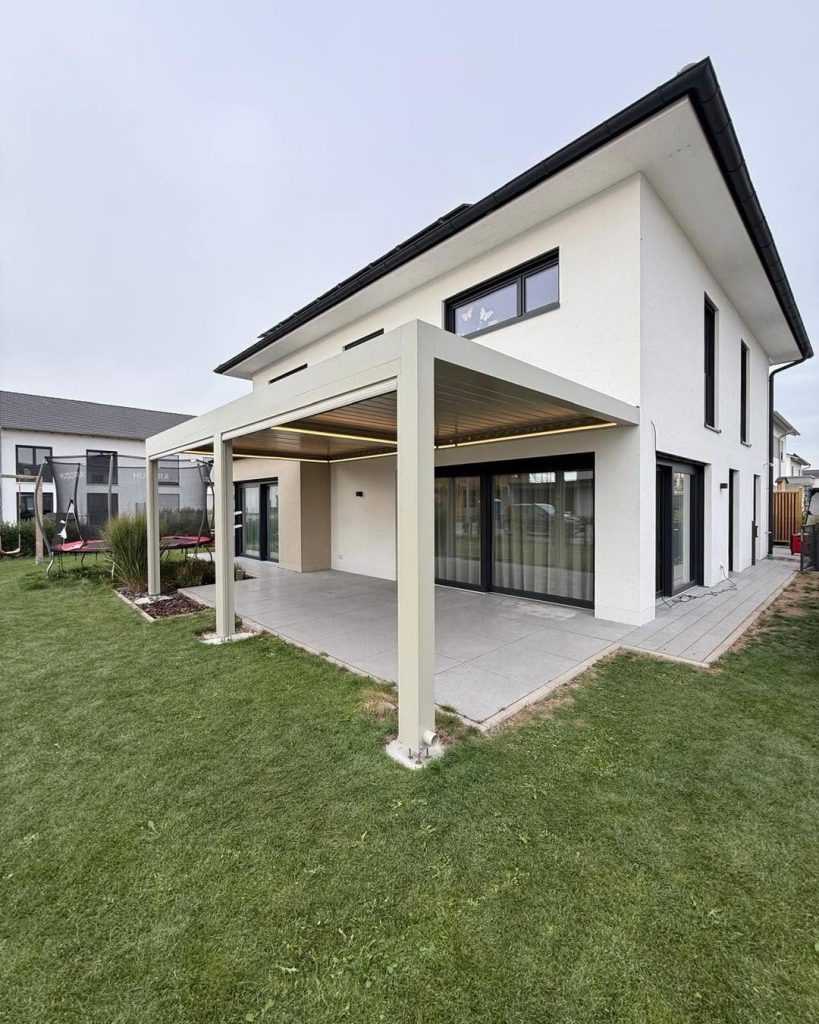 Beigefarbene Pergola in Schwabmünchen über der Terrasse eines modernen Hauses mit großen Schiebetüren