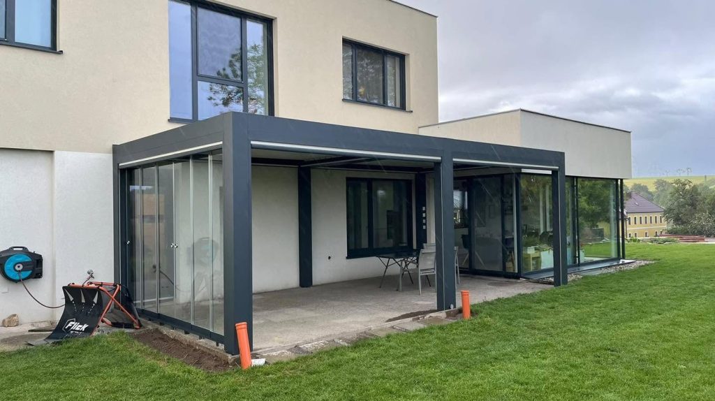 Lamellendach mit Glasschiebewänden an der Gartenseite eines Hauses mit Flachdach