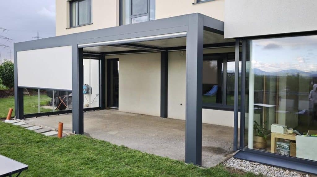 Anthrazitfarbenes Lamellendach mit Glaswand an einem modernen Haus mit großen Fenstern