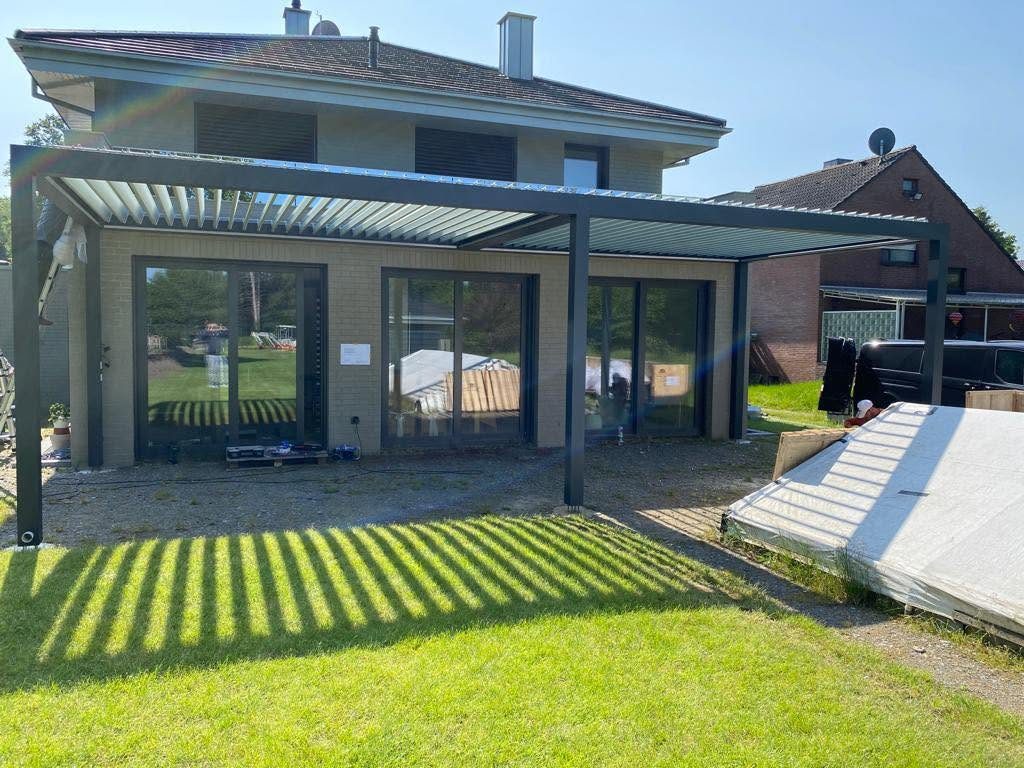 Lamellendach in Hünxe vor großen Schiebetüren eines Hauses, auf dem Rasen fallen die Schatten der Lamellen