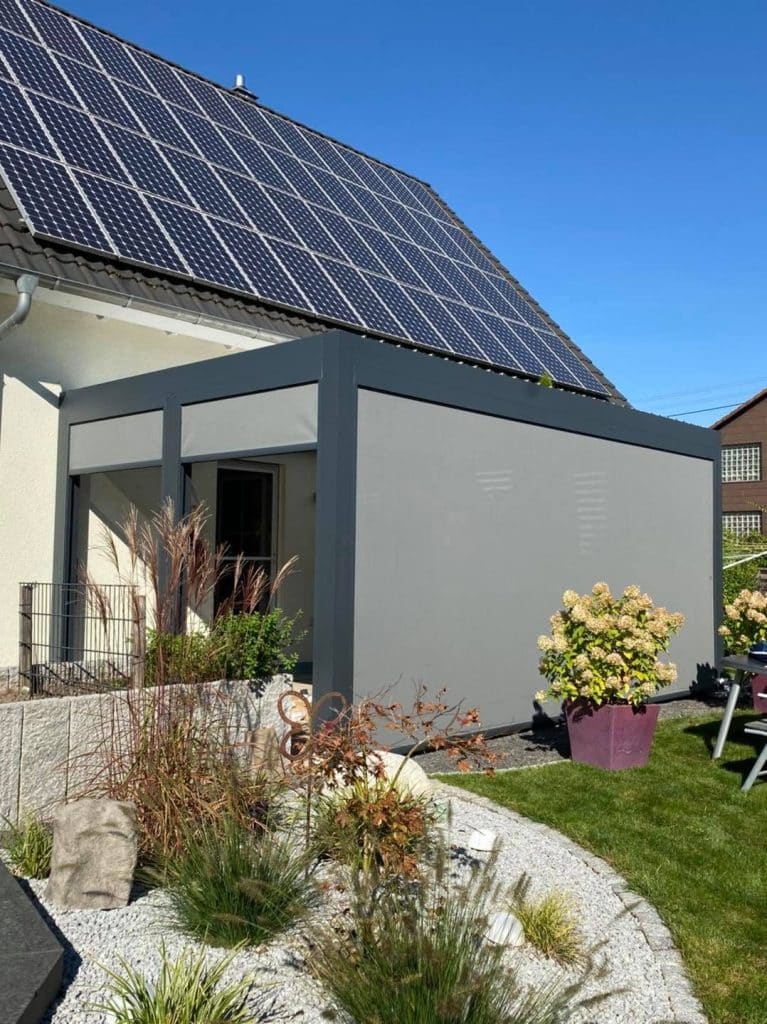 Haus mit Photovoltaik-Dach und Pergola mit Screen, im Vorgarten ein Beet mit Ziergräsern