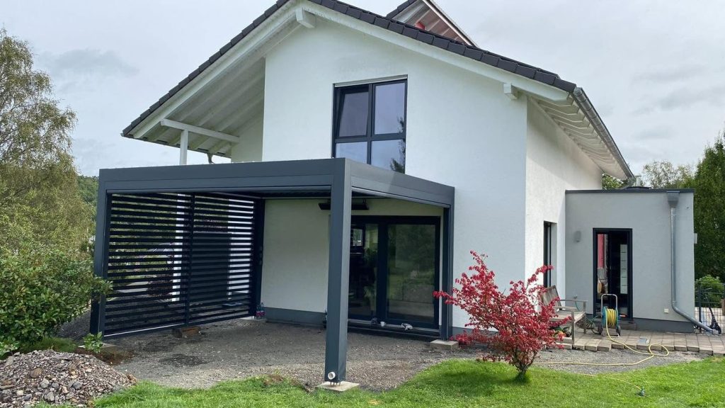 Anthrazitfarbene Pergola in Siegen am Haus mit Zierstrauch, die Seite ist mit einer Lamellenwand geschlossen