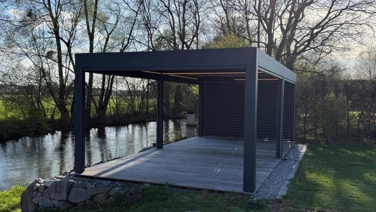 Anthrazitfarbene Pergola in Marchtrenk mit Holzterrasse direkt am Wasser, daneben Bäume ohne Laub