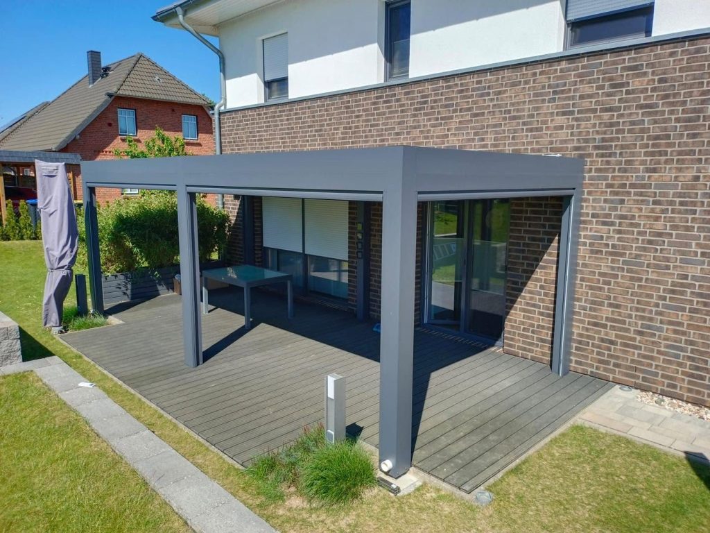 Pergola in Mecklenburg-Vorpommern auf einem Holzdeck am Klinkerhaus, im Garten ein Rasen mit Plattenweg