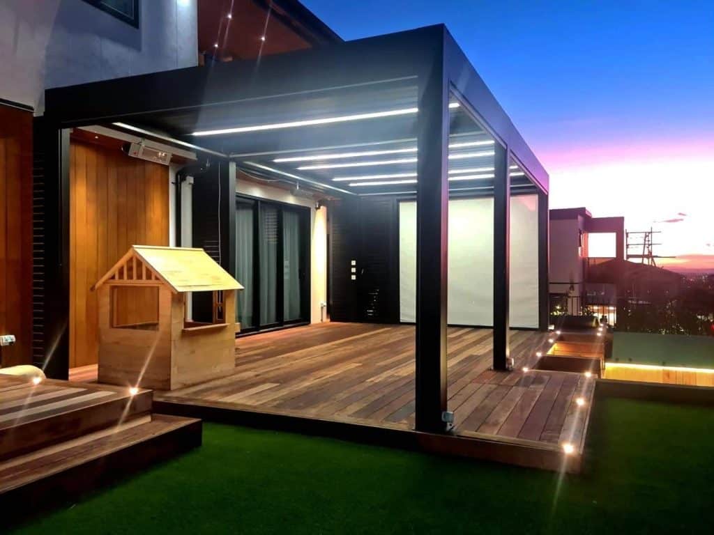 Lamellendach in Ungarn mit Holzdeck und einem Kinderspielhaus in der Dämmerung, die Terrasse ist beleuchtet