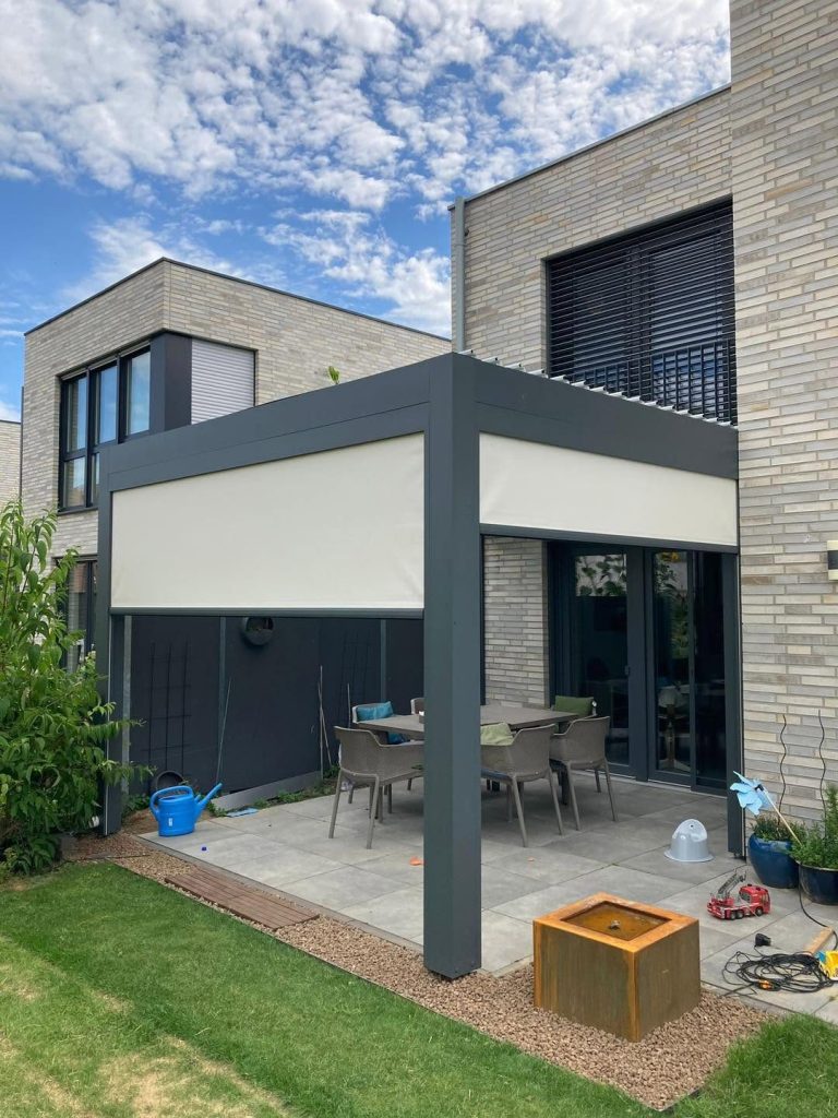 Pergola an einem Haus mit Klinkerfassade, auf der Terrasse eine Sitzgruppe und eine Feuerschale