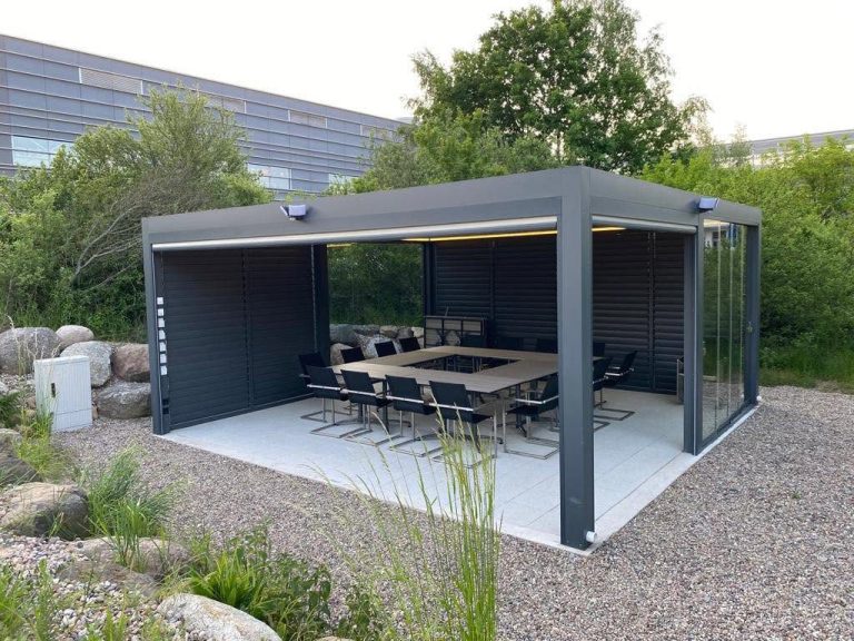 Pergola in Frankfurt (Oder) mit Lamellenwand auf der Rückseite, darunter ein Konferenztisch, davor ein Kiesbeet mit Gräsern
