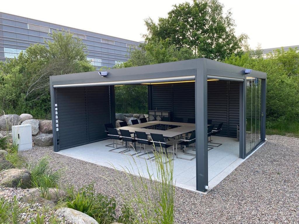 Pergola in Frankfurt (Oder) mit Lamellenwand auf der Rückseite, darunter ein Konferenztisch, davor ein Kiesbeet mit Gräsern