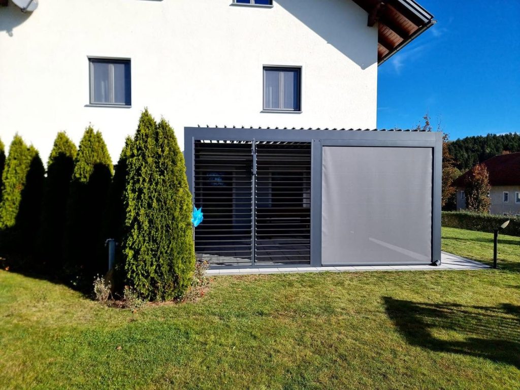 Lamellendach in Oberösterreich mit Lamellenwand und Screen an einem Haus, davor Thujen und Rasen