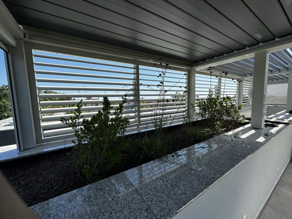 Weiße Lamellenwand mit Hochbeet aus Granit unter einem Lamellendach auf der Dachterrasse