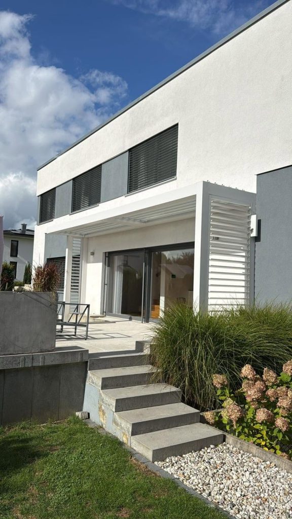 Weiße Lamellenwand an der Terrasse eines modernen Hauses, die Steintreppe führt zum Garten