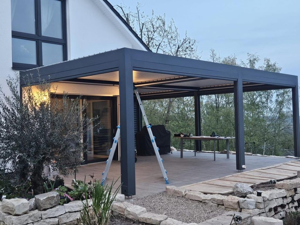 Anthrazitfarbene Pergola in Köln mit LED-Licht über einer Terrasse am Hang, davor Natursteine