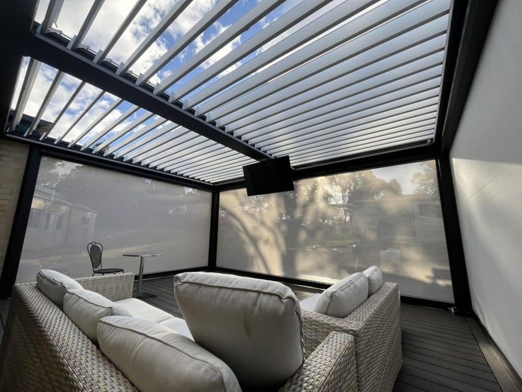 Lounge mit Korbmöbeln und Fernseher unter einem Lamellendach in Hessen mit geöffneten Lamellen