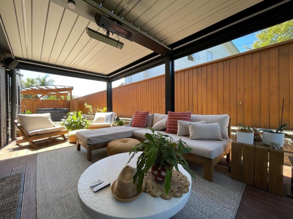 Lounge mit Sofa und Heizstrahler unter einem Lamellendach in Ungarn, hinter dem Sofa eine Holzwand