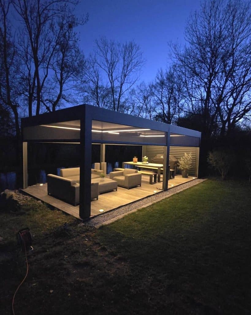 Pergola mit Loungemöbeln und warmem LED-Licht in der Dämmerung, im Garten stehen kahle Bäume