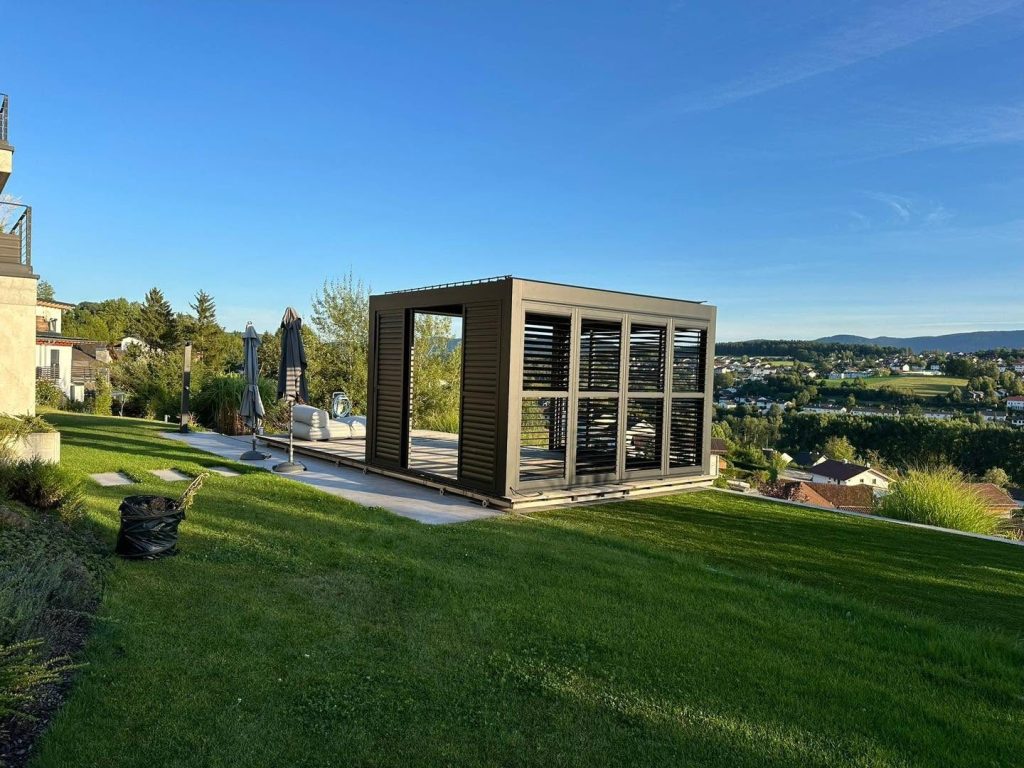 Pavillon in Bayern mit Lamellendach und Lamellenwänden im Garten, dahinter eine weite Hügellandschaft