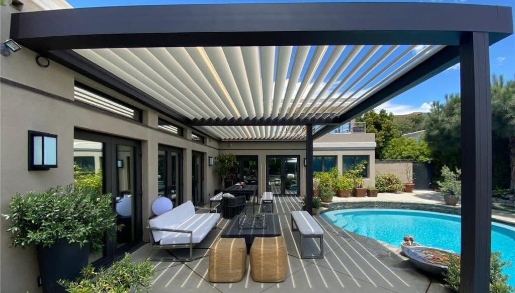 Lamellendach mit geöffneten Lamellen über einer Terrasse mit Pool, Sitzgruppe und Esstisch