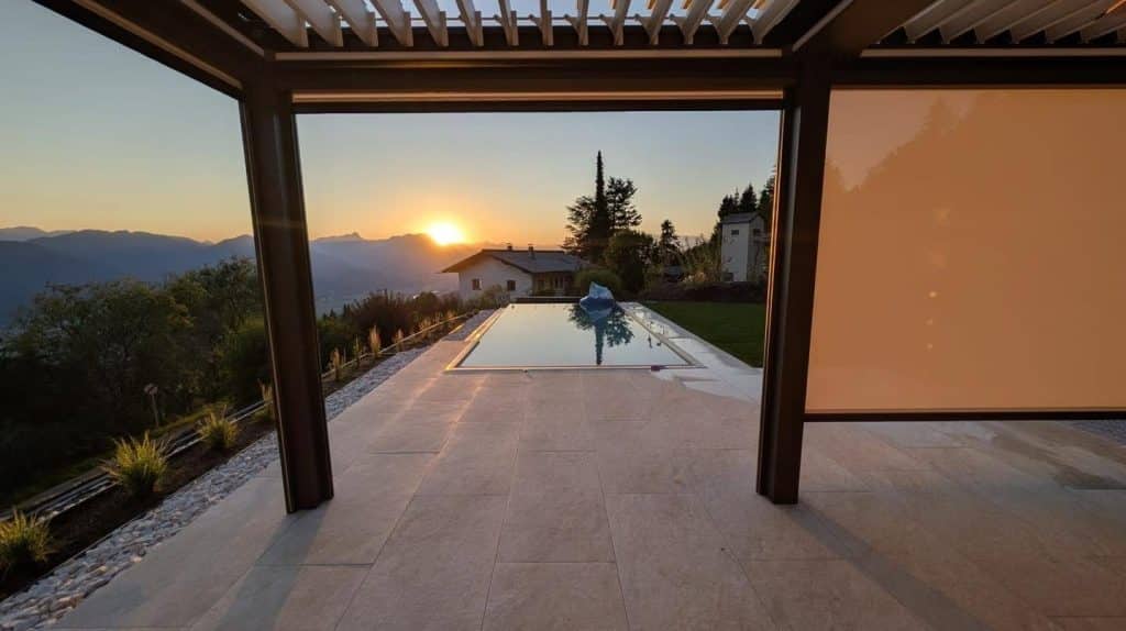 Blick unter ein Lamellendach in Kärnten auf den Pool und den Sonnenuntergang über den Bergen