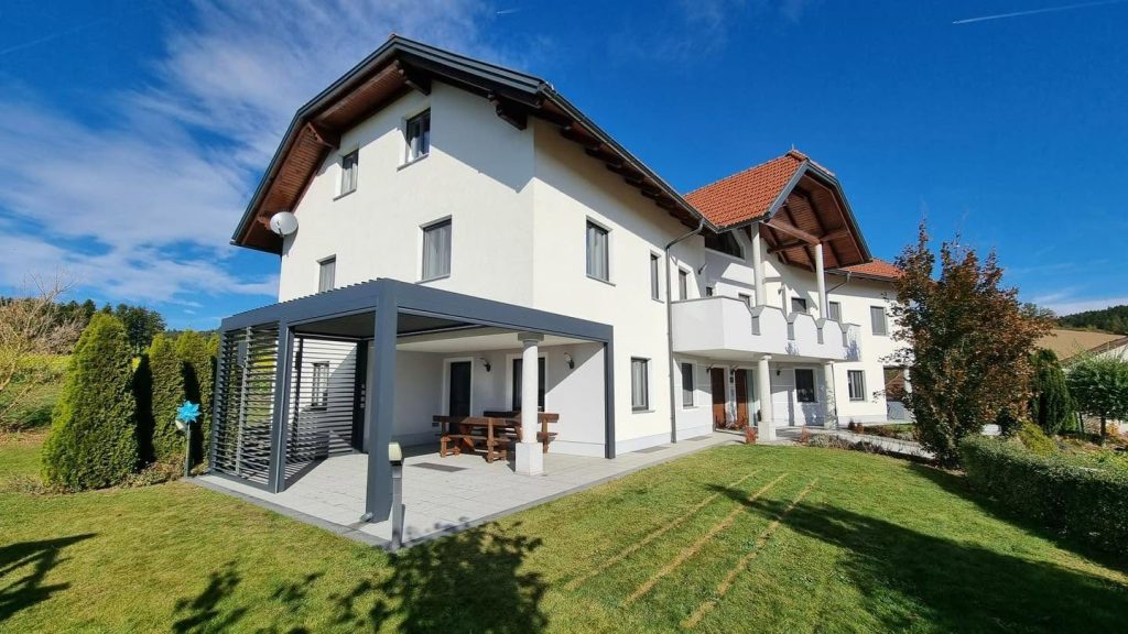 Lamellendach in Oberösterreich an einem weißen Wohnhaus mit Balkonen, davor ein Rasen und ein Terrassenbereich