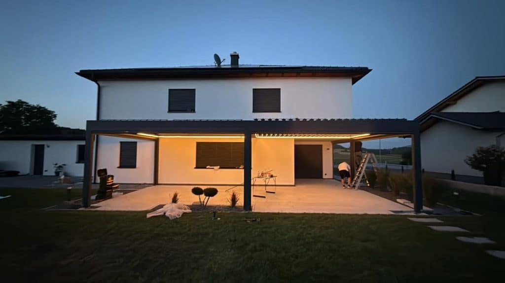Wohnhaus mit Lamellendach in Cham und warm beleuchteter Terrasse in der Dämmerung